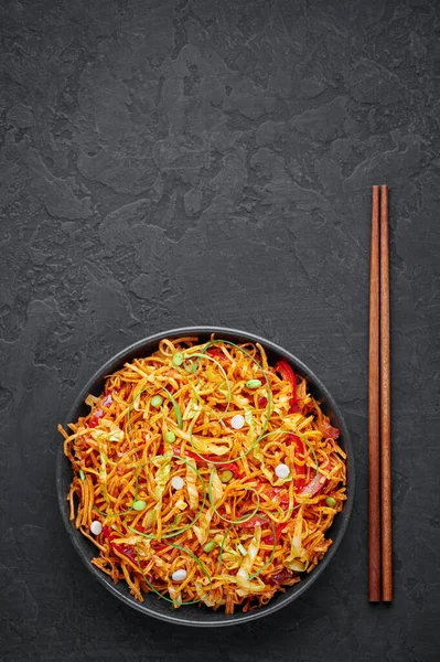 暗いスレートテーブルの上に黒いボウルに中国語のベル 中華料理の鉄板焼中華料理の屋台料理です深い揚げ客麺 野菜やSchezwanソース — ストック写真