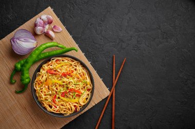 Siyah kâse içinde kırmızı biberli sarımsaklı Hakka Eriştesi. Hint-Çin vejetaryen yemek tabağı. Sebzeli Hint eriştesi. Klasik Asya yemeği. Uzayı kopyala Üst görünüm