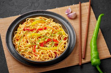 Siyah kâse içinde kırmızı biberli sarımsaklı Hakka Eriştesi. Hint-Çin vejetaryen yemek tabağı. Sebzeli Hint eriştesi. Klasik Asya yemeği.