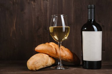Kahverengi ahşap zemin üzerinde ekmek şişesi ve şarap kadehi olan beyaz şarap kompozisyonu