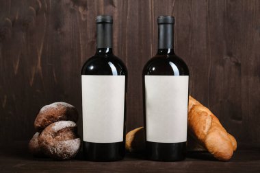 Ekmek, iki şişe ve kahverengi ahşap arka planda şarap kadehiyle beyaz şarap kompozisyonu.