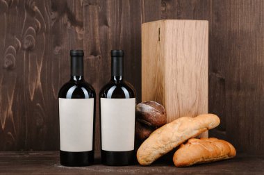 Ekmekli şarap kompozisyonu, kutuda iki şişe ve kahverengi ahşap arka planda şarap kadehi.
