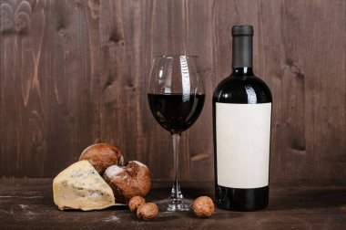 Ekmekli kırmızı şarap kompozisyonu, kutuda iki şişe ve kahverengi ahşap arka planda şarap kadehi.