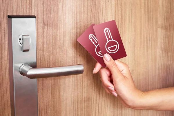 two hotel red key cards in woman\'s hand. Locked wooden door with silver handle.