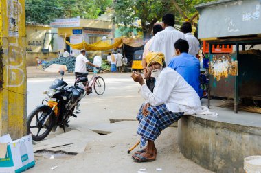 Yaşlı Hintli adam markette oturur ve sigara içer. 11 Şubat 2018 Puttaparthi, Hindistan