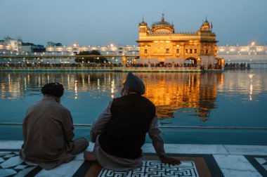Two indian sikhs mans sits near the water of golden temple at night. 24 february 2018 Amritsar, India.