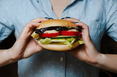 Vejetaryen hamburgeri siyah arka planda kadın ellerini tutuyor.