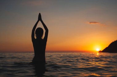 Yoga kadın gün batımı silueti pozu denizde. Güneş doğarken okyanus banyosu