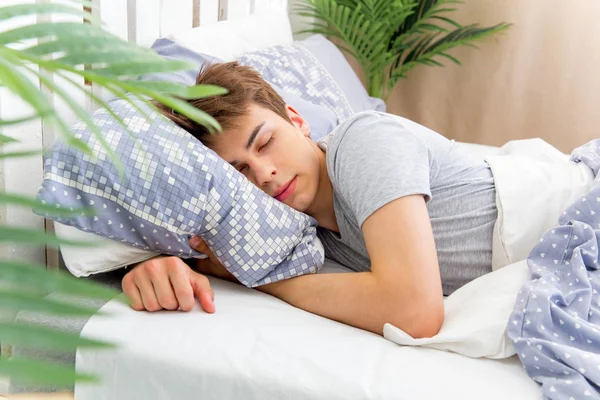 Bonito jovem dormindo em roupa de cama branca — Fotografia de Stock