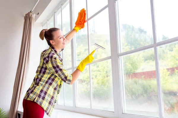 La mujer con guantes protectores sonríe y limpia el polvo con un aerosol y un plumero — Foto de Stock