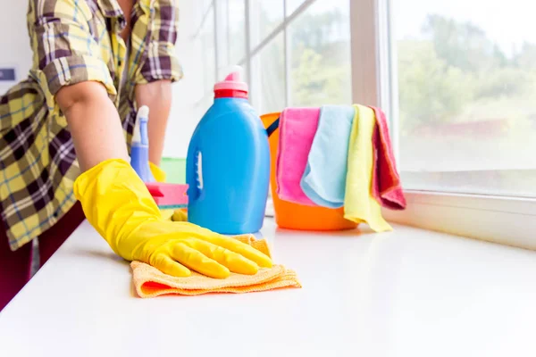 La mujer con guantes protectores sonríe y limpia el polvo con un aerosol y un plumero —  Fotos de Stock