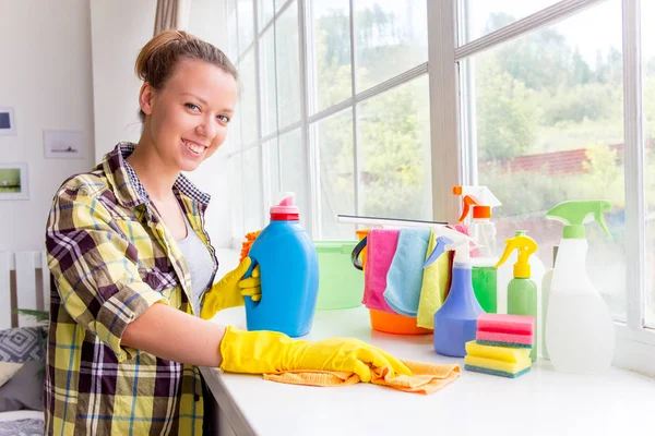 La mujer con guantes protectores sonríe y limpia el polvo con un aerosol y un plumero — Foto de Stock