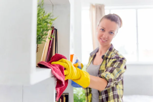 La mujer con guantes protectores sonríe y limpia el polvo con un aerosol y un plumero — Foto de Stock