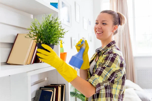 La mujer con guantes protectores sonríe y limpia el polvo con un aerosol y un plumero — Foto de Stock