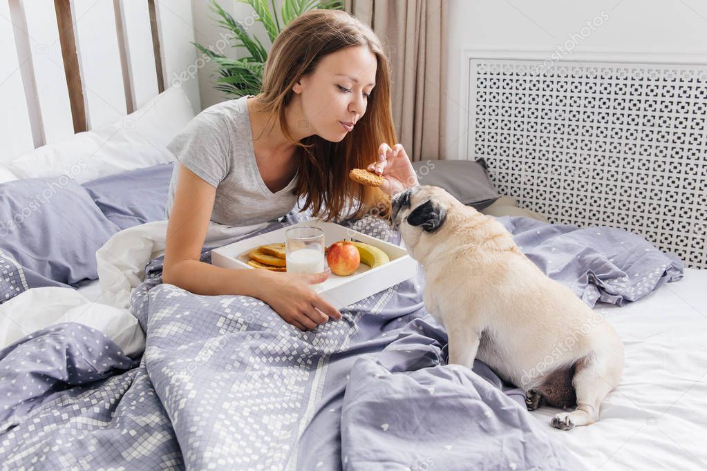 Young woman with her dog in a bed. Breakfast in bed