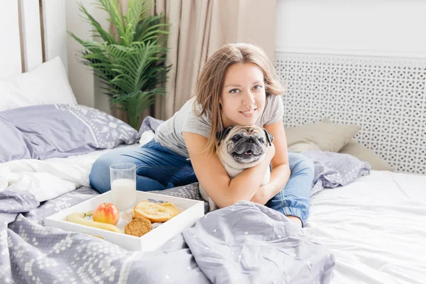 Ung kvinna med hennes hund i en säng. Frukost på sängen — Stockfoto