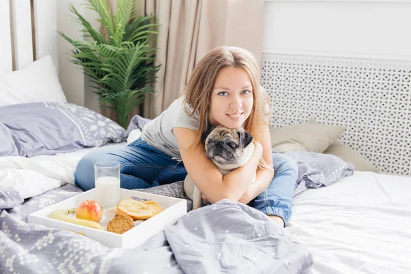 Ung kvinna med hennes hund i en säng. Frukost på sängen — Stockfoto