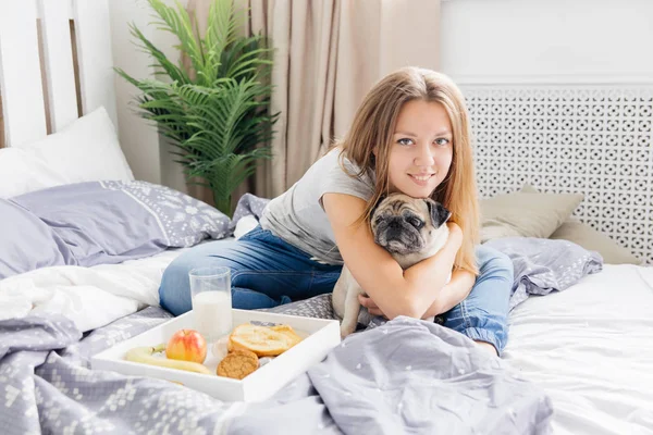 Ung kvinna med hennes hund i en säng. Frukost på sängen — Stockfoto