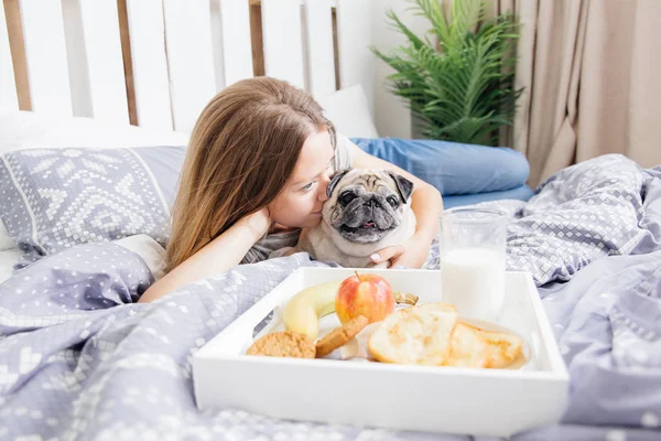 Ung kvinna med hennes hund i en säng. Frukost på sängen — Stockfoto