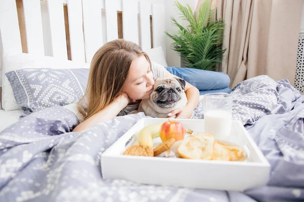 Ung kvinna med hennes hund i en säng. Frukost på sängen — Stockfoto