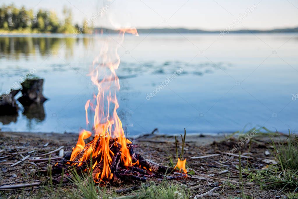 Beautiful campfire in the evening at lake. Fire burning in dusk at campsite near a river in beautiful nature