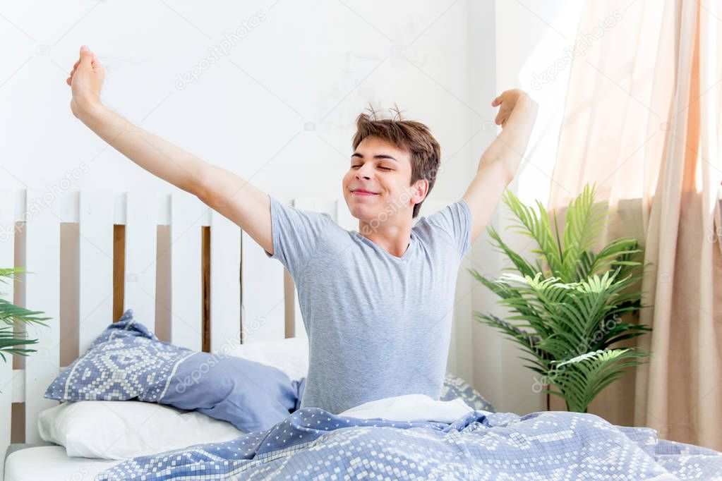 A young man waking up in bed in the morning