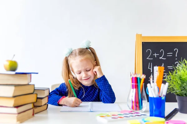 Zadowolony ładny pracowity dziecko siedzi przy biurku w pomieszczeniu — Zdjęcie stockowe