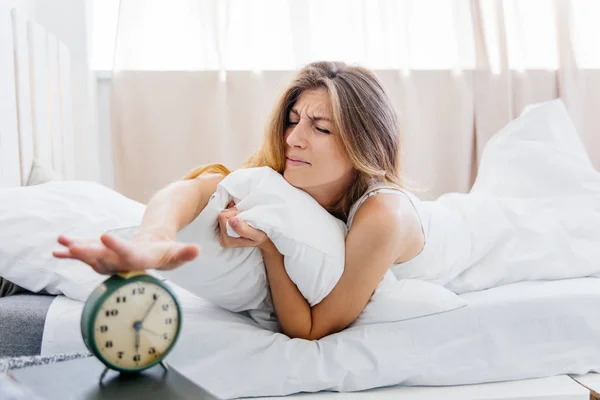 Young woman turns off the alarm clock in the morning