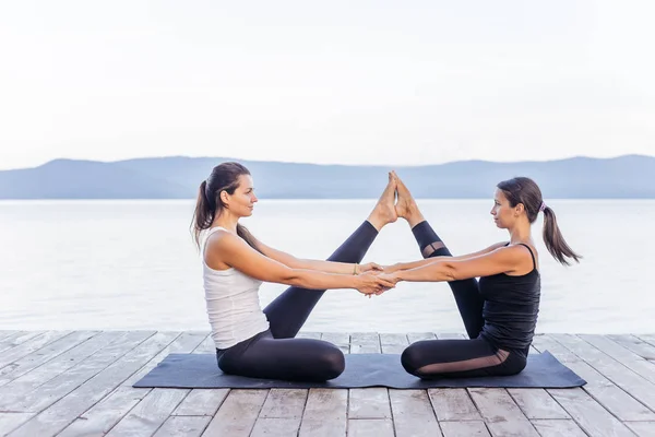 Giovani donne attraenti sorridenti che praticano yoga su un lago — Foto Stock