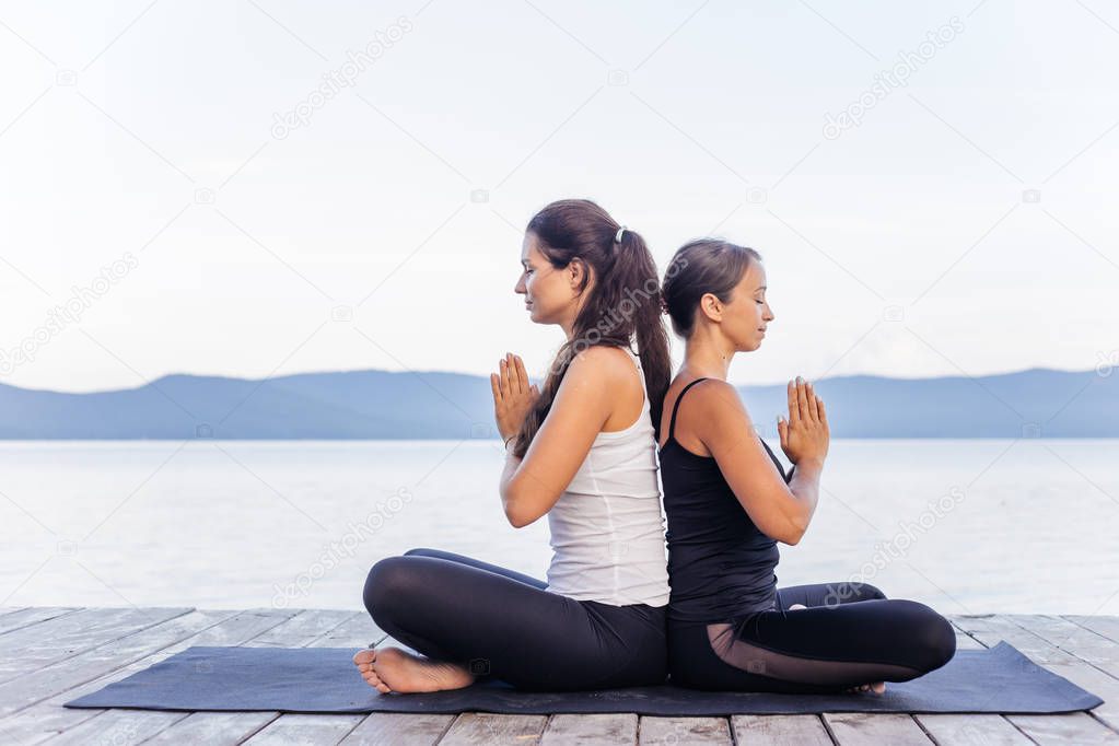 Young attractive smiling women practicing yoga on a lake