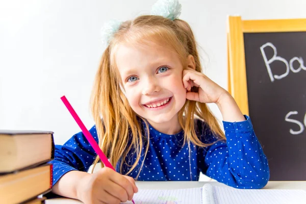 Happy cute industrious child is sitting at a desk indoors — Stock Photo, Image