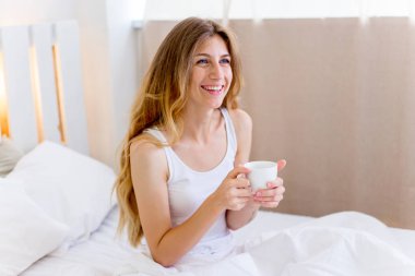 Genç ve güzel bir kadın yatakta kahvaltı yapıyor.