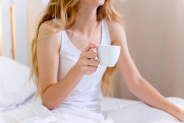 Genç ve güzel bir kadın yatakta kahvaltı yapıyor.