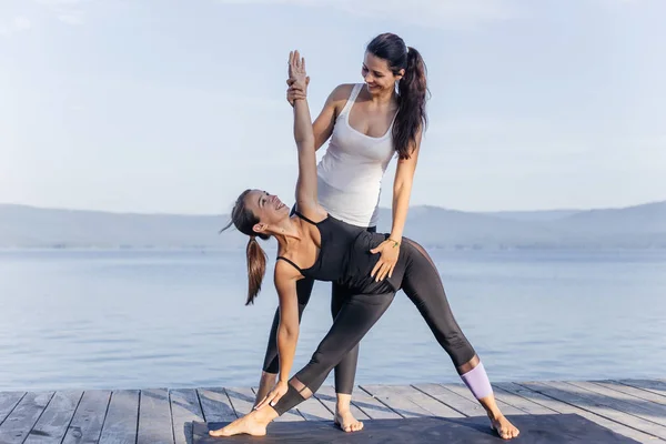 Giovani donne attraenti sorridenti che praticano yoga su un lago — Foto Stock