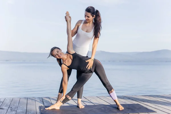 Giovani donne attraenti sorridenti che praticano yoga su un lago — Foto Stock