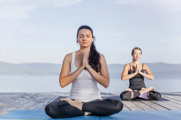 Jonge aantrekkelijke glimlachende vrouwen beoefenen van yoga op een meer — Stockfoto