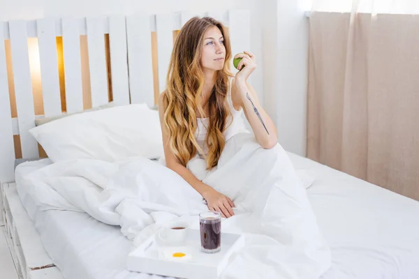 Genç ve güzel bir kadın yatakta kahvaltı yapıyor. — Stok fotoğraf