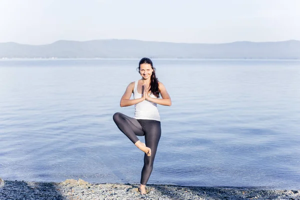 Giovane donna attraente sorridente che pratica yoga su un lago — Foto Stock