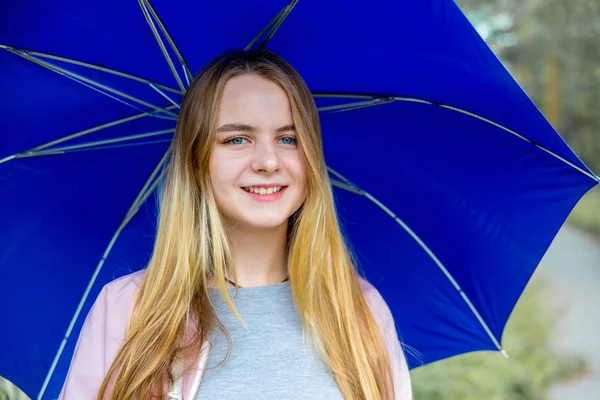 Joven mujer de pie bajo el paraguas azul bajo la lluvia —  Fotos de Stock
