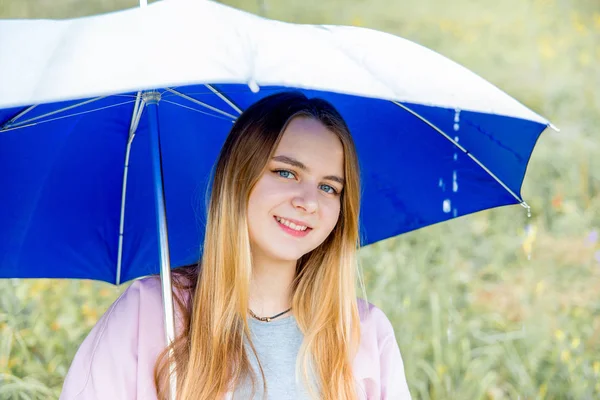 Joven mujer de pie bajo el paraguas azul bajo la lluvia —  Fotos de Stock