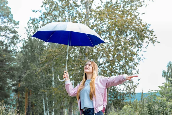 Mladá žena stojí pod modrý deštník v dešti — Stock fotografie