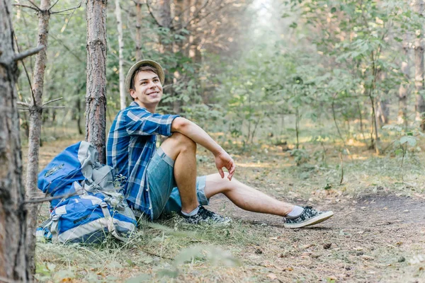 Jovem caminhante do sexo masculino está sentado e descansando na floresta — Fotografia de Stock