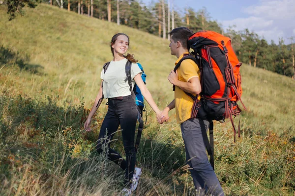 Casal de turistas com mochilas caminhando até uma montanha — Fotografia de Stock