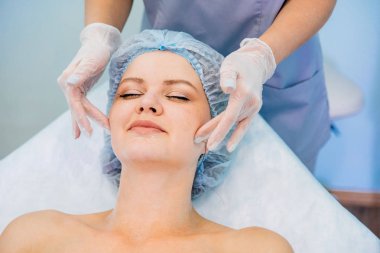 Genç ve güzel bir kadın yüz masajı yaptırıyor.