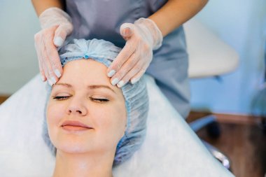 Genç ve güzel bir kadın yüz masajı yaptırıyor.