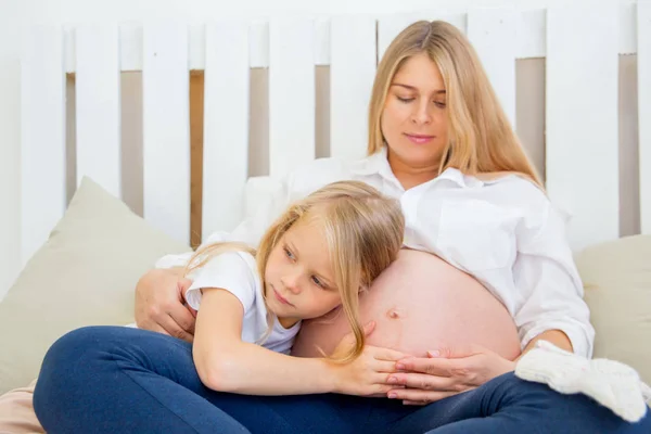 Szczęśliwy uśmiechający się matki w ciąży, przytulanie się z córką w domu — Zdjęcie stockowe