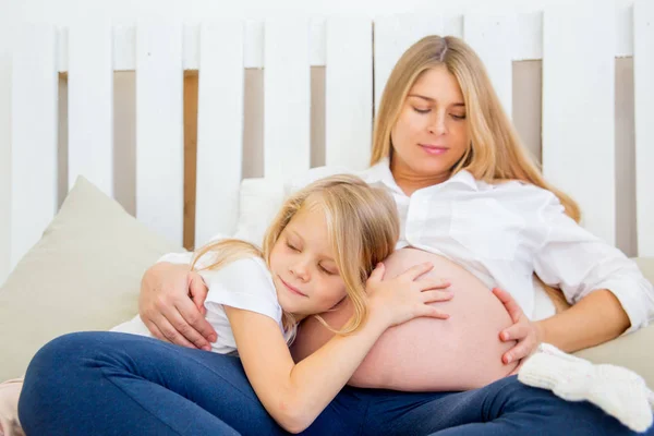 Feliz sonriente madre embarazada abrazando con su hija en casa — Foto de Stock