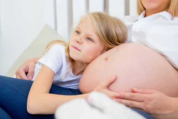 Щаслива усміхнена вагітна мати обіймає з дочкою вдома — стокове фото