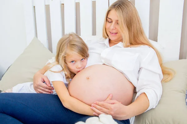 Szczęśliwy uśmiechający się matki w ciąży, przytulanie się z córką w domu — Zdjęcie stockowe