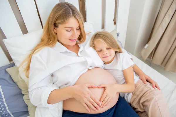 Glücklich lächelnde schwangere Mutter umarmt ihre Tochter zu Hause — Stockfoto